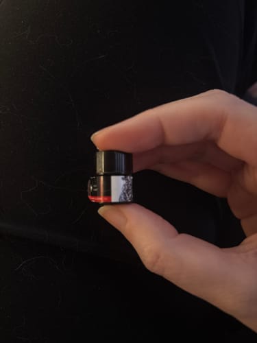 Close-up of a reviewer holding a tiny sample bottle of Cold Heart perfume between their fingers.
