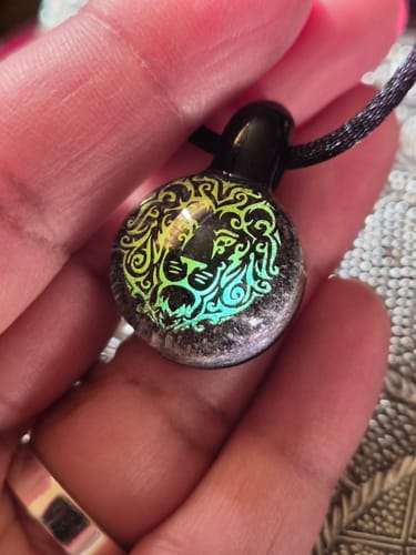 Close-up of a reviewer's hand holding the round Lion Hologram Pendant with infused ash.