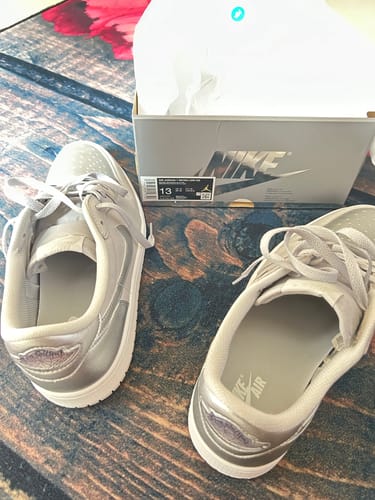 A customer's pair of silver sneakers displayed next to their open shoebox on a patterned floor.