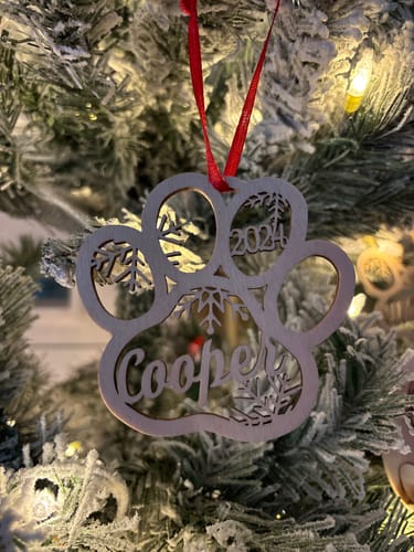 Customer's personalized wooden paw-print ornament with 'Cooper' and '2024', hanging on a Christmas tree.