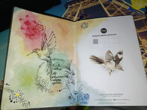 Customer's open Weekly 2026 Planner, showing personalized pages with drawings, stickers, and colorful watercolor art.