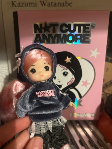 Customer holding the Little Mimi doll with pink hair and a dark hoodie in front of the album's pink packaging.