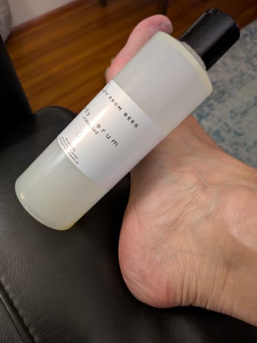 A reviewer holds the Body Serum bottle against their foot, illustrating its use on dry heels.