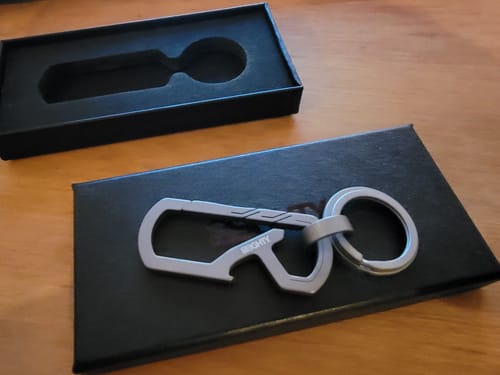 Customer's 80Eighty Titanium Keychain Clip resting on its black case, with the open box behind it.