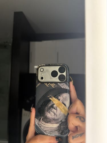 A reviewer's mirror selfie showing a custom iPhone case with a dollar bill graphic and a gold brushstroke accent.