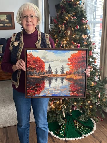 Reviewer holding a completed Custom Paint by Numbers Kit showing a vibrant autumn lake scene.