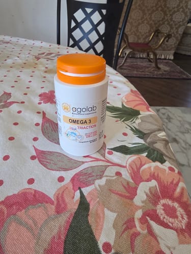 Recensore mostra la bottiglia bianca di Omega 3 con tappo arancione, posata su un tavolo.