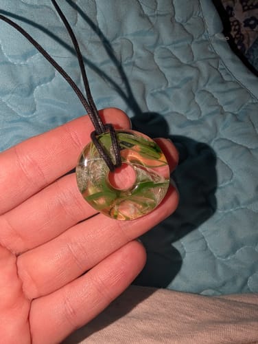Customer holds their Taffy Confetti Halo Pendant. The clear resin pendant has colorful swirls inside.