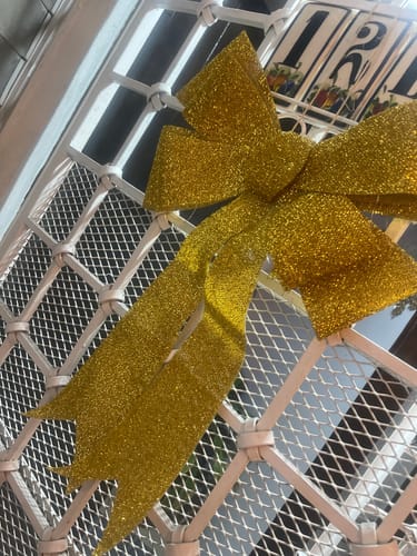 Un cliente muestra el moño navideño dorado brillante colgado en una reja blanca.