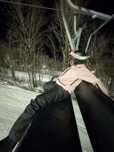 Reviewer wearing the pink snow jacket while sitting on a ski lift at night.