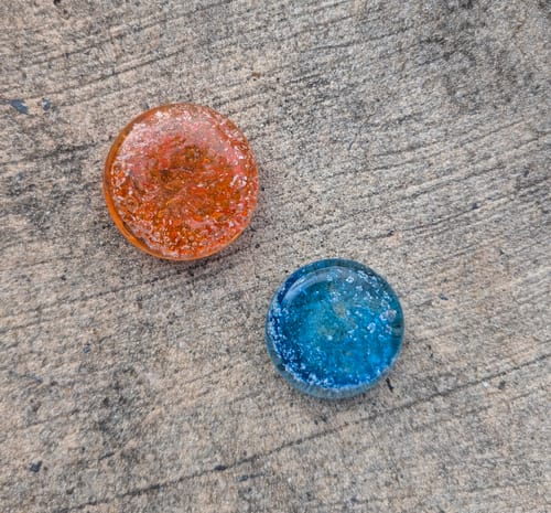 Customer's two round Soul Stones, one orange and one blue, resting on a gray stone surface.