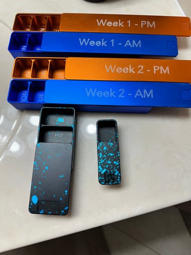 Reviewer's assortment of Weekly AM-PM Vitamin Cases in blue, orange, and a black splatter design.