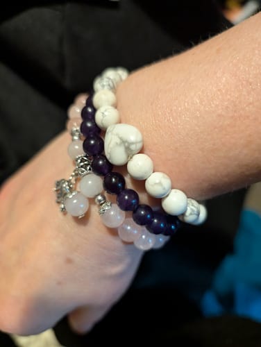 Reviewer's wrist with a white crystal bracelet featuring a heart bead, stacked with other crystal bracelets.