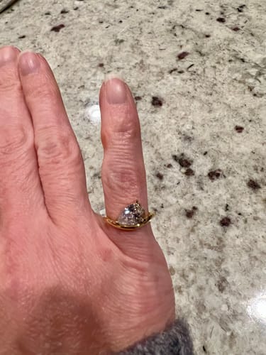 Customer wearing the gold Pia Ring with a pear-cut stone on their pinky finger against a granite countertop.