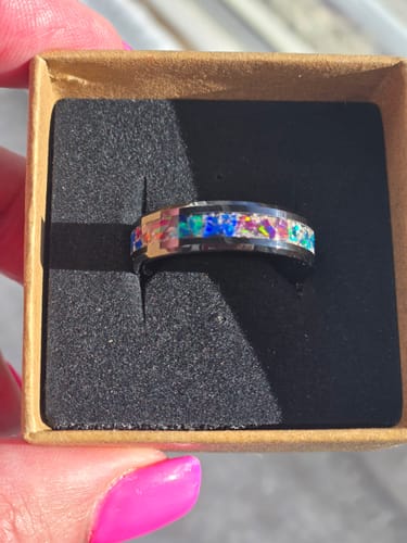 Customer holding open a box to show a Titanium Carbide Ring with a colorful, sparkling cremation ashes inlay.