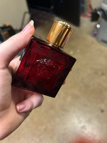 Customer holding the red glass bottle of Eros Flame For Men By Versace perfume with a gold cap.