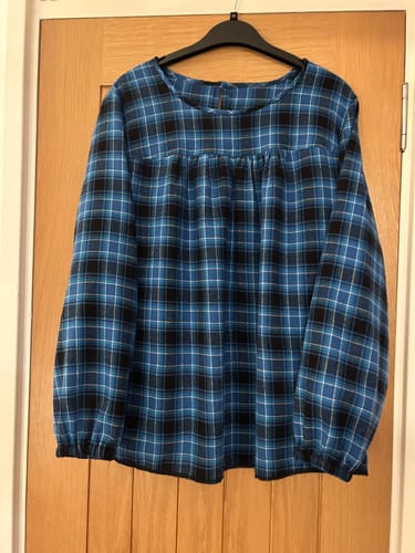 Reviewer's cosy top made from the blue, black, and white tartan fabric, hanging on a black hanger against a door.