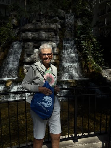 A happy reviewer smiles while standing in front of a scenic waterfall during an outing.