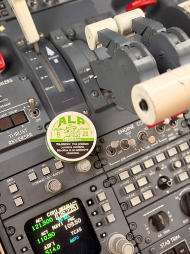 Reviewer's can of Spearmint Nicotine Pouches sitting on the control panel of an airplane cockpit.