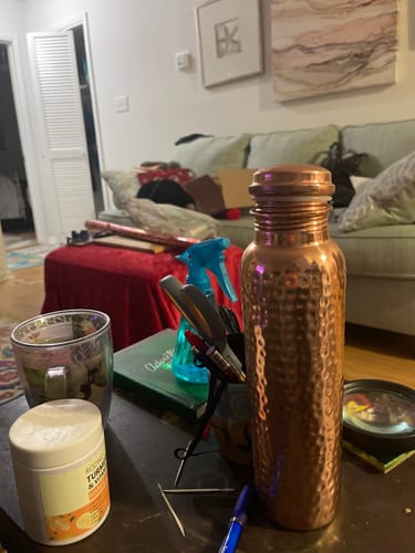 Customer's hand-hammered copper water bottle sitting on a cluttered table in a living room.