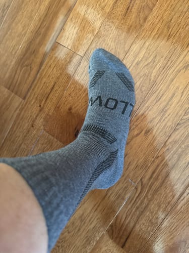 Customer wearing a grey Men's Alpaca crew sock on their foot indoors.