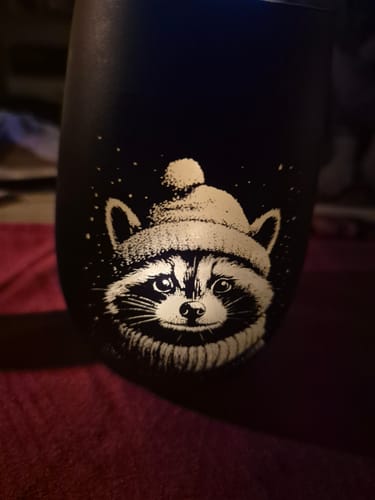 Kunde zeigt eine Nahaufnahme des schwarzen Windlichts mit einem detaillierten Waschbär-Motiv mit Mütze.