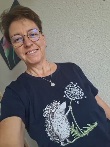 Kundin trägt das dunkle Premium Bio-Shirt mit dem Aufdruck 'Igel mit Pusteblume'.