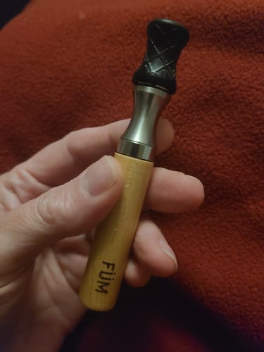 Customer holding the Füm device, showing its wooden body and textured black mouthpiece against a red background.