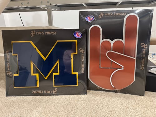 Customer's 'Hook'em Horns' wall art in its packaging, placed on the floor next to another team's sign.