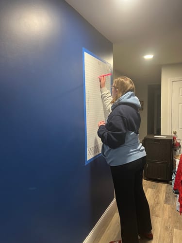 Reviewer writing on the ELF Giant Word Search Puzzle taped to a blue wall in a hallway.