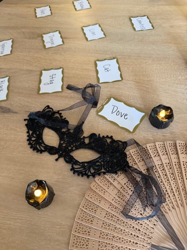 Customer's table set for the Masquerade Ball Murder Mystery game, showing a black mask, fan, and character name cards.