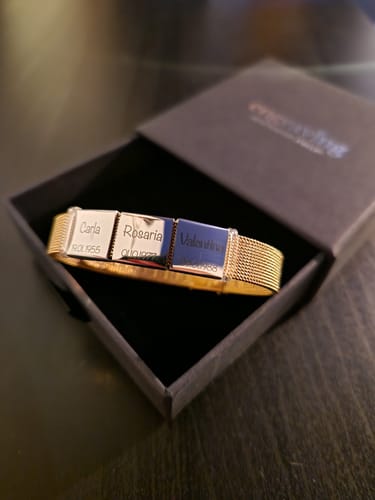 Customer's gold Lux bracelet with three engraved pendants, displayed in its black gift box.