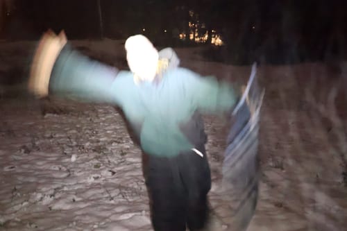 Partial view of a reviewer in motion wearing the dark green snow jacket in a snowy setting at night.