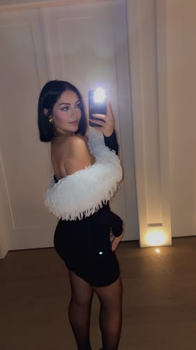 Reviewer taking a selfie in the black Butter Off-Shoulder Feather Dress, showing the white feather trim from a side angle.