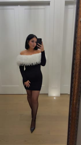 Reviewer in a full-length mirror selfie wearing the black Butter Off-Shoulder Feather Dress with sheer tights.