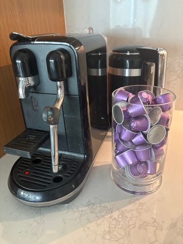 Customer's purple Blend 12 coffee capsules in a glass container next to a black coffee machine.