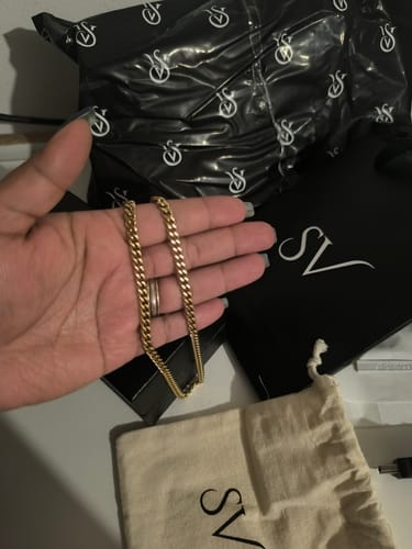 Cliente sosteniendo la Cadena Miami Cuban Oro en la palma de su mano, con el empaque de la marca al fondo.