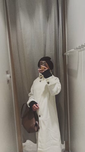 Reviewer takes a mirror selfie wearing the white Juliana Stand Collar Long Coat in a fitting room.