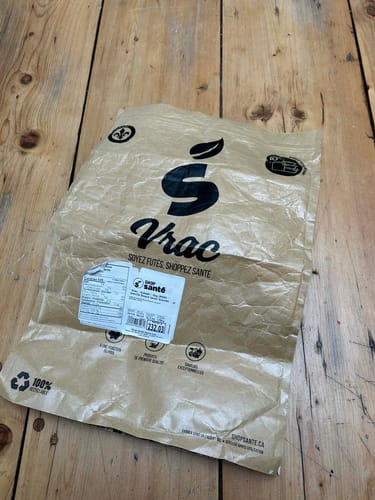 Sac en papier brun du client pour la protéine Vrac - Isolate, posé sur une surface en bois.