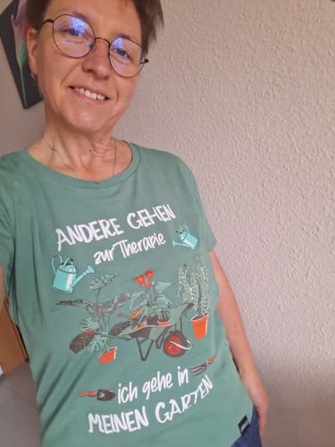 Eine Kundin trägt lächelnd das grüne 'Garten Therapie' Premium Bio-Shirt.