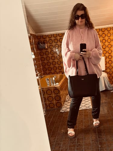 Kundin trägt den kuscheligen, rosafarbenen Oversized-Cardigan "CozyGlam", kombiniert mit einer schwarzen Hose.