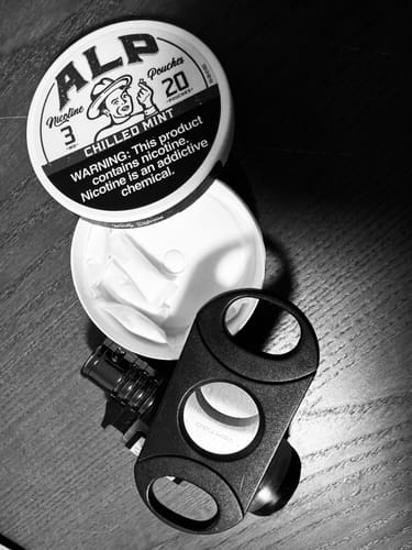 Reviewer's black and white photo of an open can of Chilled Mint Nicotine Pouches on a dark wooden surface.