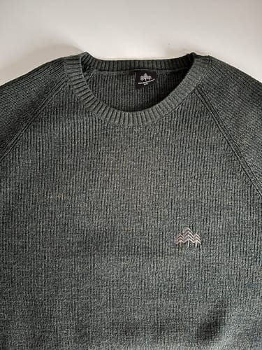 Kunde zeigt den dunkelgrauen Strickpullover 'Lodge' in einer Nahaufnahme, die den Kragen und das Logo hervorhebt.