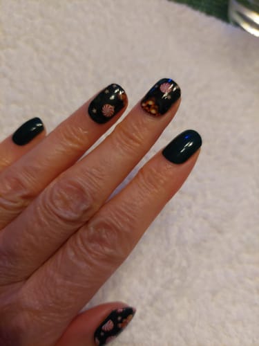 Hand einer Kundin mit einer Maniküre, die einfarbig tiefgrüne Evergreen Dream Nägel mit festlich verzierten Akzentnägeln kombiniert.