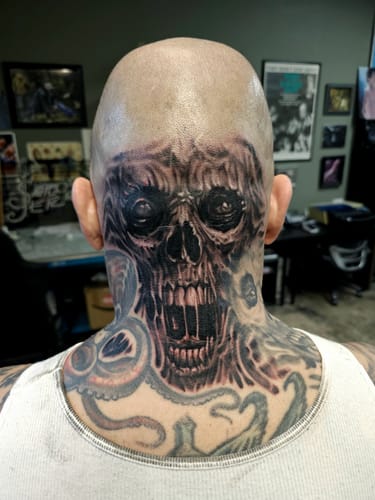 Reviewer shows a large skull tattoo on a client's head and neck, done using Painless Tattoo numbing cream.
