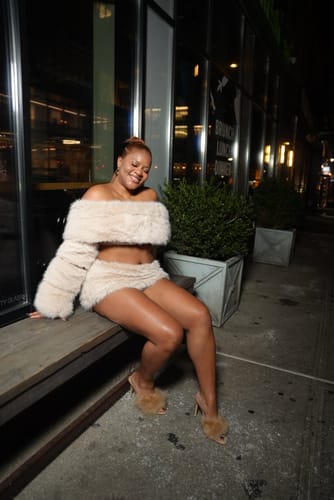 Reviewer sitting on an outdoor bench at night, wearing the Faux Fur Pelted Off-Shoulder Top and matching skirt.