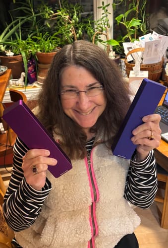 Reviewer smiling while holding a purple and a blue rectangular case from the 2-Pack Bundle.