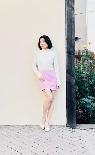 Reviewer posing outdoors in the pink Suiting Mini Skirt paired with a white top and heels.