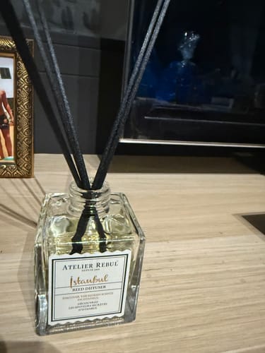 Recensent toont de Istanbul Geurstokjes in een vierkante glazen fles op een houten oppervlak.