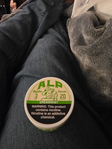 A customer's can of ALP Spearmint Nicotine Pouches resting on their lap.